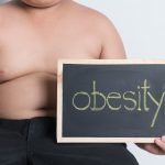 A fat boy holding a blackboard saying obesity