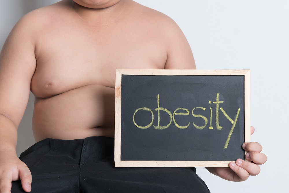 A fat boy holding a blackboard saying obesity