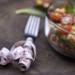 Measuring tape wrapped around fork next to a salad bowl