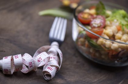 Measuring tape wrapped around fork next to a salad bowl