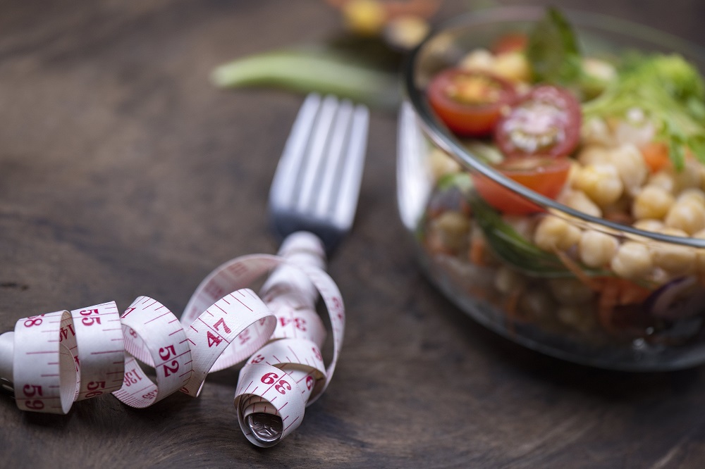 Measuring tape wrapped around fork next to a salad bowl