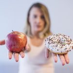 young woman choosing between donut and apple